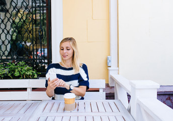 young woman sending a text message from her cell phone in cafe. Woman using smart phone on the wooden table in outdoor cafe