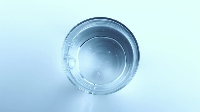 filling a glass with water through bottle on white background, view top, nutrition and health-care concept