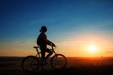 Silhouette of cyclist and a bike on sky background