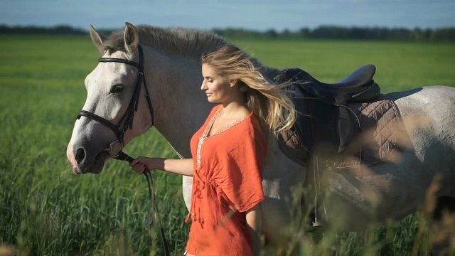 A beautiful charming blonde woman walking with a horse at a field