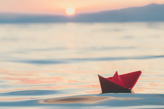 Red paper boat sailing on water at sunset. Travel and vacation concepts. 