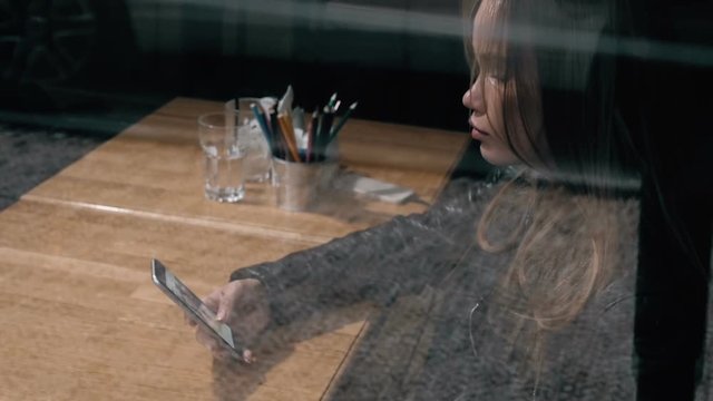 Woman at trendy cafe drinking coffee and use phone. Young beautiful Caucasian model. Reflections from windows.