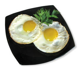 Two fried eggs on a black plate with a sprig of parsley