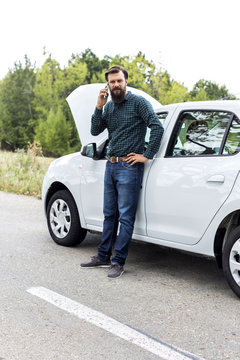  Young man using his cell phone next to a broken down car