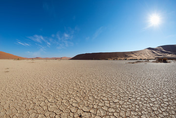 Scenic sand dunes and cracked clay pan in Sossusvlei, Namib Naukluft National Park, best tourist and travel attraction in Namibia. Adventure and exploration in Africa. Backlight with sun star.