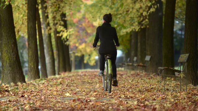 young woman rides bike away at city park in autumn fall season