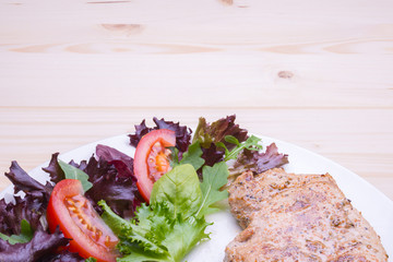 Pork steak with salad on white plate on beige wooden background,