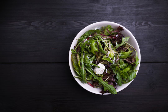 Salad lettuce with cheese in a white bowl on a dark wooden backg