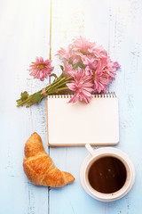 Cup of black coffee, Bouquet of flowers, fresh croissant and Empty paper sheet on Rustic blue table from above, Beautiful vintage card, Top view, copy space for text, flat lay concept