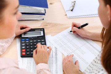 Two female accountants counting on calculator income for tax form completion hands closeup. Internal Revenue Service inspector checking financial document. Planning budget, audit  concept