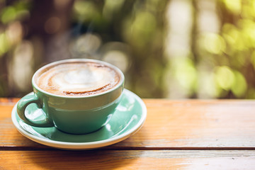 hot latte art in green cup on wooden table with book and tree.