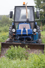 Fototapeta premium Old blue tractor stands in a meadow in the rain, front view