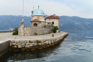 Fototapeta na wymiar Our Lady on the Rocks islet with the Roman Catholic church of Virgin Mary in the bay of Kotor, Montenegro. Peaceful morning. Beautiful high mountains surround the bay