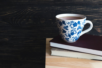Cup of hot tea and books on wooden table