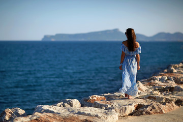 Woman walking along the sea on the rocks in the blue dress and l