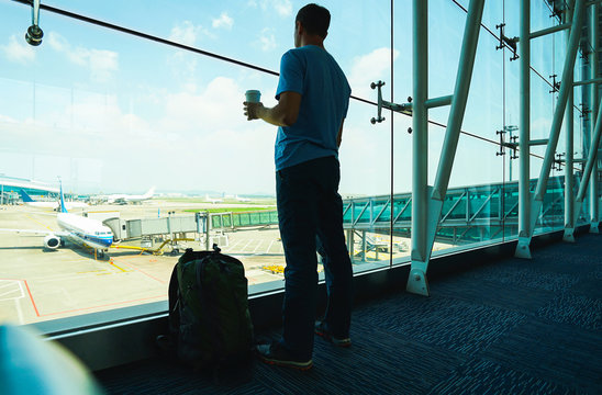 Passenger with coffee cup in hand and backpack waiting his fly in airport. Travel concept.