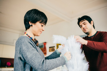 Half length of couple of young handsome caucasian man and woman unpacking christmas tree, looking downward, concentrate - christmas, holiday, winter concept