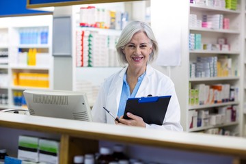 Smiling pharmacist holding a clipboard in pharmacy