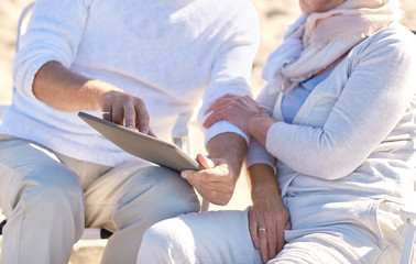 close up of senior couple with tablet pc on beach