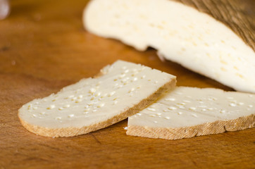 parmesan cheese sliced on olive board, over oak table.