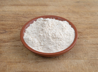 Quinoa flour in a bowl on a wood cutting board.