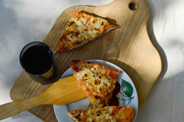 Pieces of pineapple pizza and glass cup of cola on wooden plate