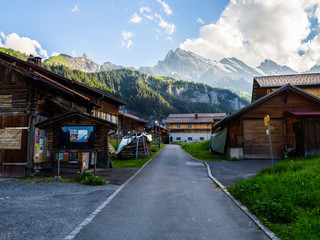 Fototapeta premium Vistas de las calles del pueblo de Gimmelwald en Suiza, entre la madera de sus granjas admirando el paisaje con montañas y nubes al fondo, viajando en verano de 2016