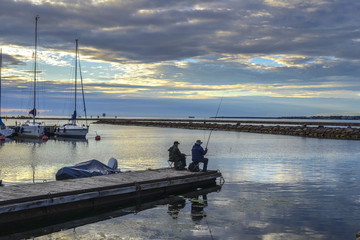 ESTONIA, TALLIN: Two anglers fishing on a cloudy evening with setting sun from a pier in the yacht harbor of Tallinn, capital of Estonia