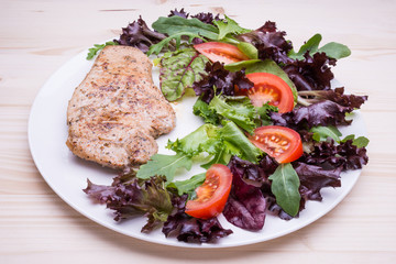 Beef steak with tomato and salad on white plate on beige wooden
