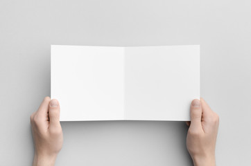 Square Bi-Fold Brochure Mock-Up - Male hands holding a blank bi-fold on a gray background.