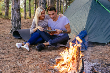 Young caucasian couple camping in the forest. Hikers in the wood near the tent with campfire, ukulele guitar, map and compass. 