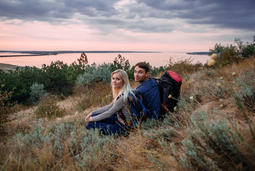 Fototapeta na wymiar Young caucasian couple hiking outdoors with backpacks during sunset