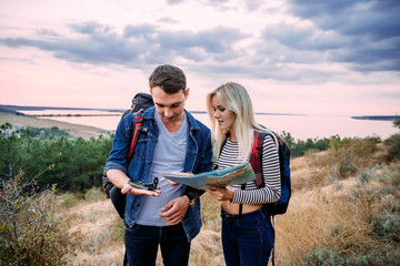 Young couple hiking with map and compass, trying to find a way. Hikers in countryside during sunset