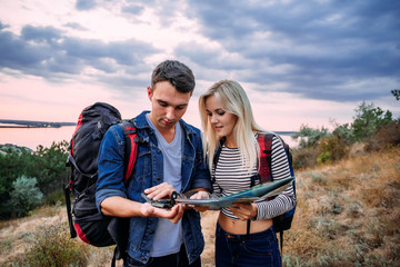 Young couple hiking with map and compass, trying to find a way. Hikers in countryside during sunset