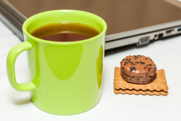 Biscuits and tea in green cup with laptop as background