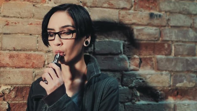Gothic woman with short black hair smokes an electronic cigarette on a background of a brick wall in an abandoned house