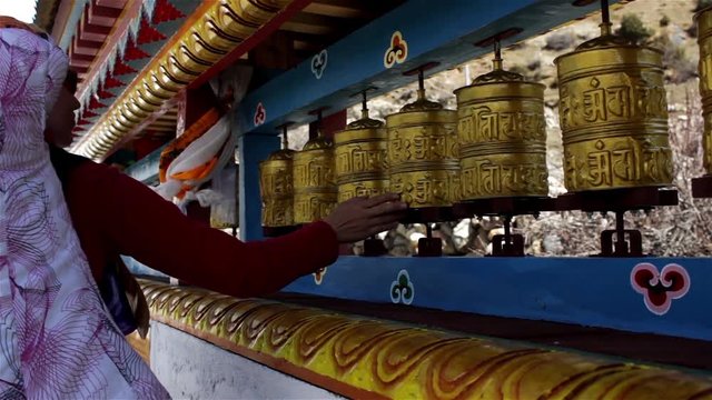 Caucasian trekker woman spins golden prayer wheels in front of Buddhist monastery on Annapurna circuit trek in Nepal