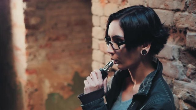 Gothic young woman smokes an electronic cigarette in an abandoned house near the brick wall