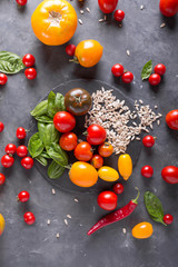 Tomatoes of different varieties, basil, sunflower seeds on a slate on a gray background