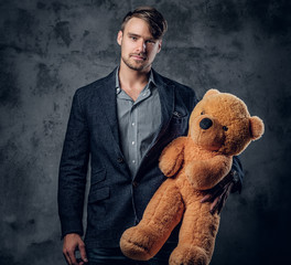 Male in a suit holding brown teddy bear.