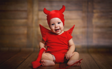 funny baby in devil halloween costume on wooden background