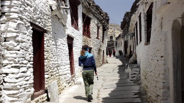 Woman travelling in Asia walks along paved narrow street between white stone houses. Old architecture of poor asian people