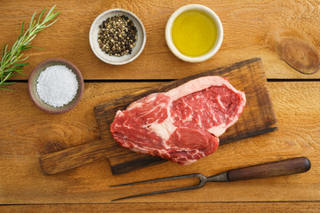 Uncooked rib eye steak on wooden board on wood