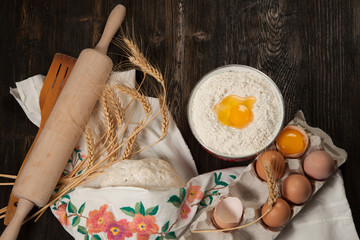ingredients for homemade bread on vintage wooden background and towel with embroidered ears of wheat, milk, eggs, flour, dough, bread