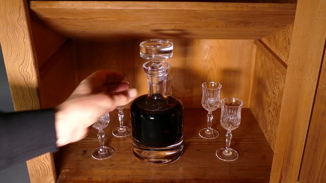 Forward slide of a hand opening an old pine cupboard to remove an alcohol decanter and a glass.