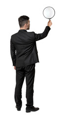 Fototapeta premium Back view of a businessman holding big magnifying glass in his outstretched arm isolated on white background