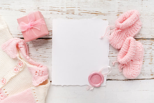 Baby Girl Clothes, Blank Card With Wax Seal And Small Present Box On White Wooden Background. Flat Lay. Owerhad View