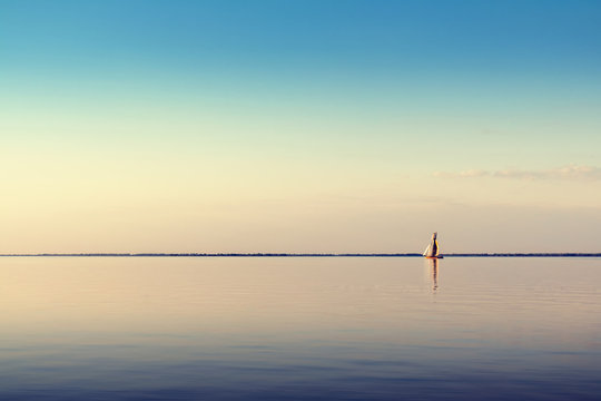 Water landscape with white sailing boat on calm waters in the light of the sunset. Toned and processing photos.