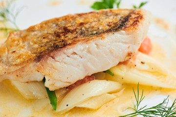 Pike perch fillet with leeks and beurre Blanc served in a white plate closeup