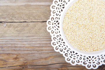 White quinoa on white plate on brown wooden background